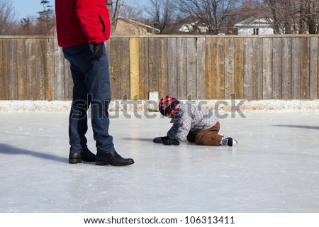 Father teaching son how to ice skate at an outdoor skating rink in winter.