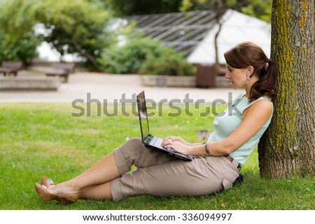 Young casual woman student in the park working on laptop