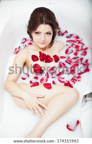 Attractive girl in bath with milk and rose petals. Spa treatments for skin rejuvenation. Alluring woman with bright makeup in Spa salon. Pretty sexy brunet relaxing in jacuzzi with red flower petals