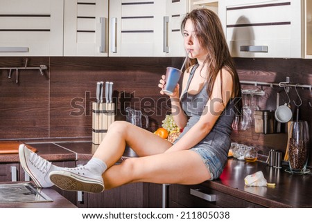 Sitting girl with cola paper glass on the kitchen desk.