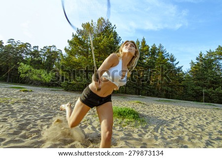 Badminton motion in a game with blond girl on sand beach