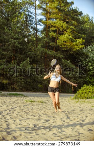 Badminton motion in a game with blond girl on sand beach