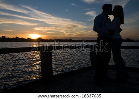 A man and woman share a kiss while the sun sets in the background