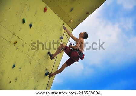 Young muscular man climbing on wall and blue sky