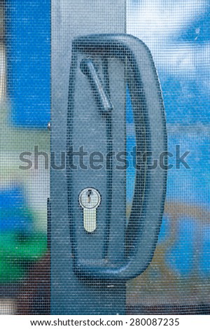 Handle and latch on open dark grey-blue sliding door behind flywire screen