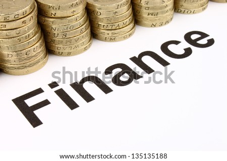 The word \'Finance\' printed black on white paper, with gold coloured coins in the background.