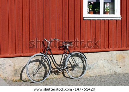 A vintage bicycle against an old red wood Scandinavian house.