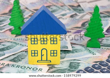 A house in Swedish colors sitting on SEK notes, with a calculator and trees.