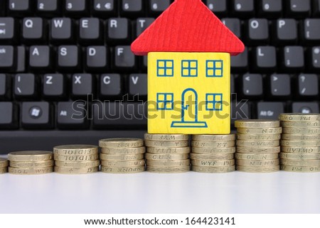 A toy house on a rising stack of coins with a computer keyboard, to symbolise searching for houses online.