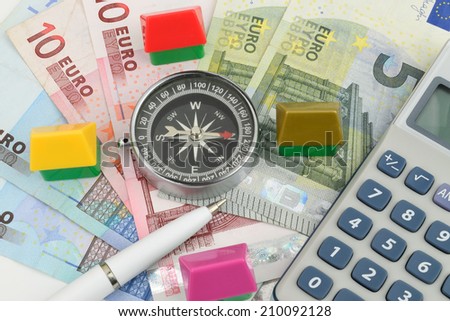 Toy houses surrounding a compass on Euro cash, a property finance metaphor.