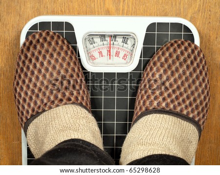 Feet in slippers standing on floor scales. Scales indicate 75 kg