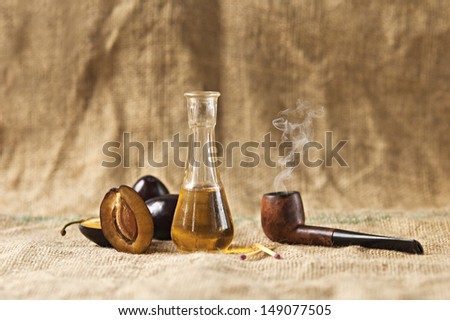 Plum brandy or schnapps with fresh and tasty plum fruit with tobacco pipe on a table cloth.