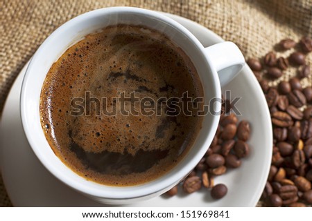Hot cup of coffee with coffee beans on canvas. Selective focus with shallow depth of field.