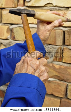 Elderly hand holding a hammer and chisel. Construction background. Selective focus on hand.