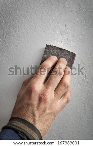 Handyman working with sandpaper on a gray wall.