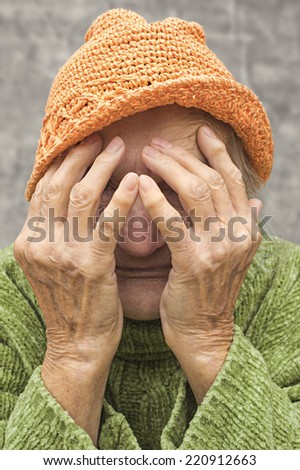 Scared and worried elderly woman covering ger face with hands.