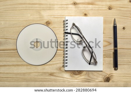 Blank stationery set : glasses, CD, notebook, and pencil on wooden table.