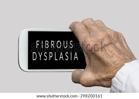 Smart phone in old hand with FIBROUS DYSPLASIA text on screen. Selective focus