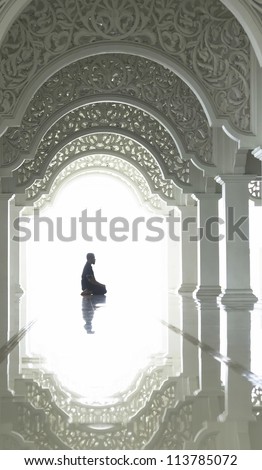 A highkey image of a Muslim prays.