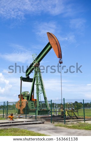 Oil pump jack in work. Oil industry in Seria, Brunei Darussalam on a sunny day with cloudy blue skies.