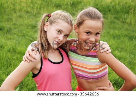 stock photo Happy preteen girls friendly hugging on green grass background