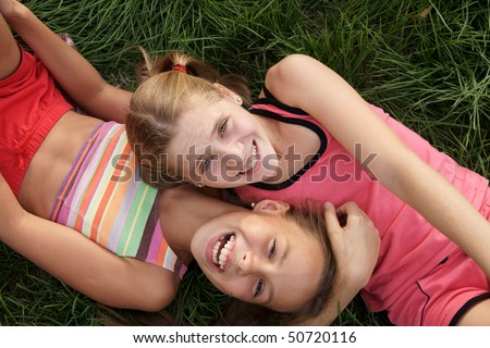 stock photo Happy preteen girls lying and playing on green grass