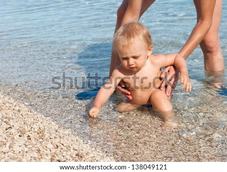 baby takes stones at the beach in mom hands