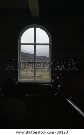 View from inside church through window.  Benches are barely visible.  Gray landscape, raindrops .