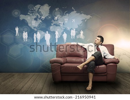 A man sitting on a couch looking a hologram depicting a network of people and transport