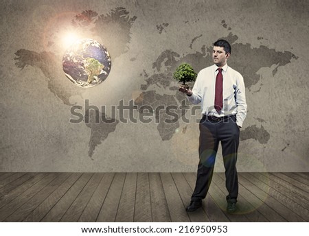 In the middle of a room a man holding a small tree thinking about the future