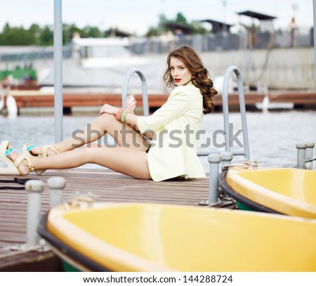 Young beautiful sexy tanned brunette woman  standing in a port fashion style, sea background, yachts