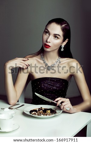 Fashion young model with red lips, luxury look n interior, sitting behind the table, eat