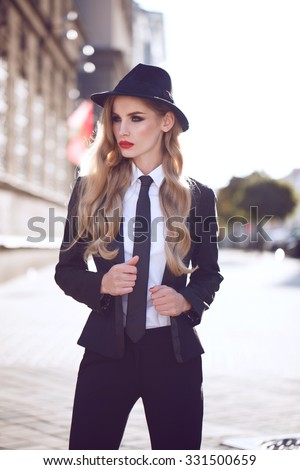 Beautiful fashion model with red lips in a classic man suit walking on the street. Outdoor.