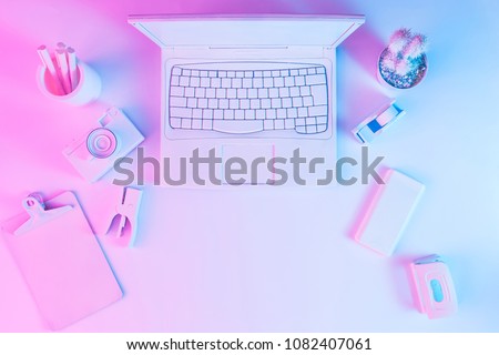 Office table with notebook computer, camera and smartphone painted in white with vibrant bold gradient purple and blue holographic color lights. Concept art. Minimal office surrealism.