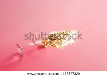 Spilled martini glass full of gold glitter on pink background. Creative minimal party concept.