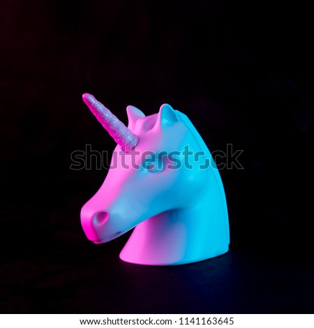 White painted unicorn head in bold pink and blue neon colors on dark background. Minimal art fantasy concept.