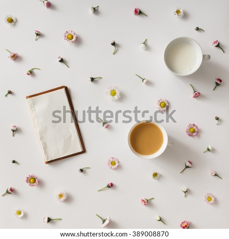 Top view of vintage notebook on white background with colorful flowers and cup of coffee and milk.