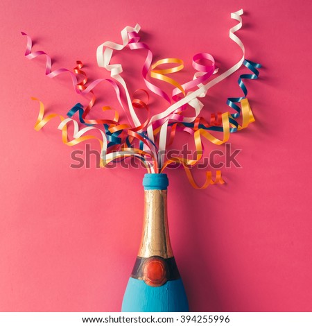 Champagne bottle with colorful party streamers on pink background. Flat lay