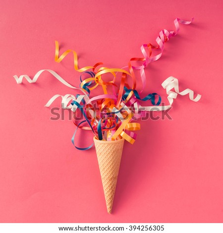Ice cream cone with colorful party streamers on pink background. Flat lay