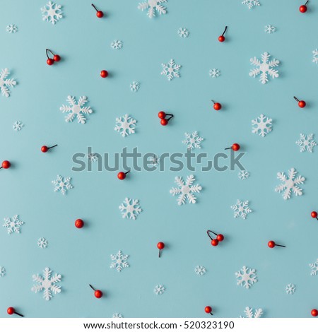 Christmas pattern made of snowflakes and red berries on blue background. Winter concept. Flat lay.