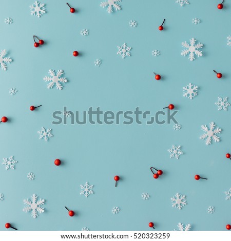 Christmas pattern made of snowflakes and red berries on blue background. Winter concept. Flat lay.