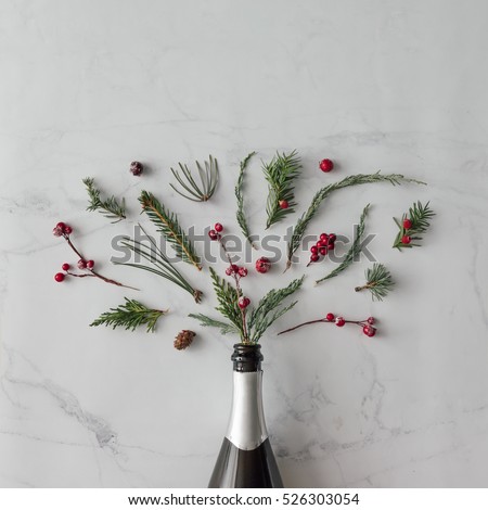 Champagne bottle with winter foliage on marble background. Flat lay. Party concept.
