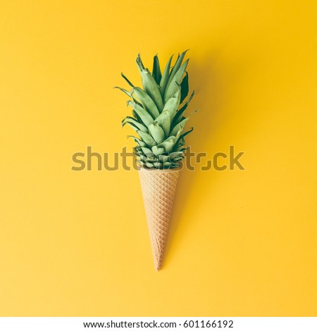 Ice cream cone with pineapple leaves on bright yellow background. Fruit and candy concept. Flat lay.