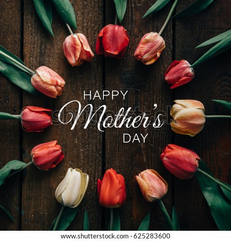 Creative arrangement of tulips on black background with happy Mothers day text. Flat lay.