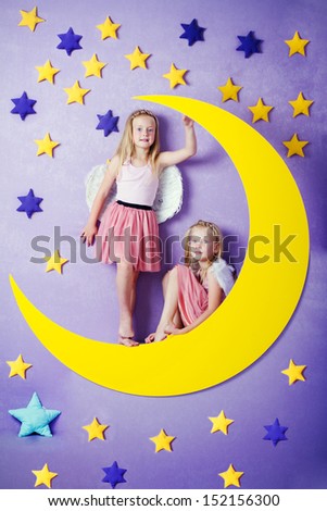 Two cute girls with angel wings sitting on a big moon