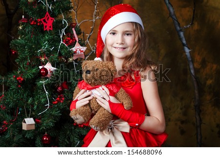 cute little girl in a red dress holding a teddy bear near a Christmas tree