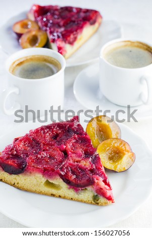 Slice of homemade plum cake on plate and two cups of coffee