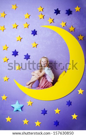 cute little girl with angel wings sitting on a big moon