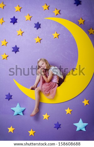 cute little girl with angel wings sitting on a big moon