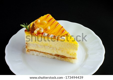 Slice of delicious mango cake on a white plate on a black background